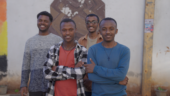 Four male students stand in a group smiling at the camera